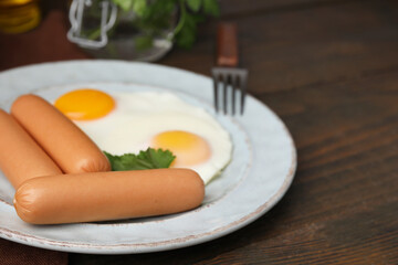 Delicious boiled sausages, fried eggs and parsley on wooden table, closeup