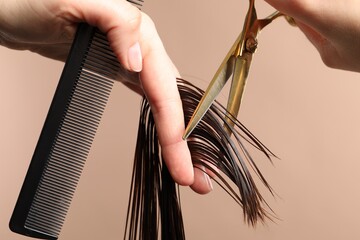 Hairdresser cutting client's hair with scissors on light brown background, closeup