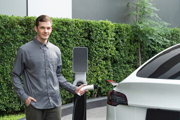 Young man travel with EV electric car charging in green sustainable city outdoor garden in summer...