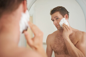 Mirror, skincare and man with shaving cream application in a bathroom for morning, routine or...