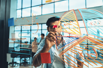 Portrait of young handsome businessman writing marketing idea by using colorful marker on glass...