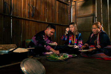 Obraz na płótnie Canvas Asian family cooking and having dinner together at home. Hill tribe man and woman in traditional dress eating food with herbal vegetable in traditional kitchen. Tribal culture and nature food concept.