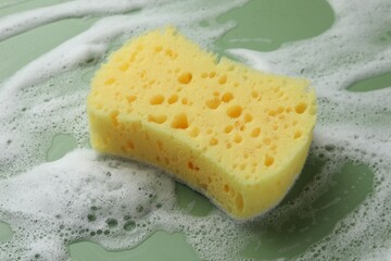 Yellow sponge with foam on green background, closeup