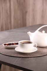 Aromatic tea in cup, saucer, teapot and dry flower petals on grey table