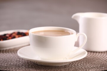 Cup of aromatic tea with milk and saucer on table, closeup