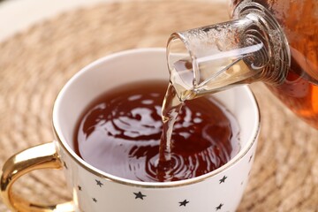 Pouring aromatic tea into cup at table, closeup