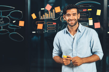 Portrait of smiling businessman standing at glass board with graph, mind map, data analysis. Happy...