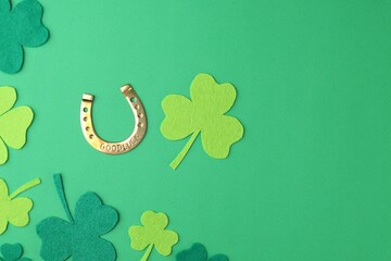 St. Patrick's day. Golden horseshoe and decorative clover leaves on green background, flat lay