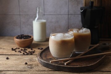 Refreshing iced coffee with milk in glasses and straws on wooden table