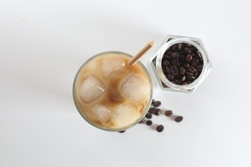Obraz na płótnie Canvas Iced coffee with milk in glass and jar of roasted beans on white background, top view