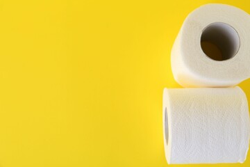 Soft toilet paper rolls on yellow background, top view. Space for text
