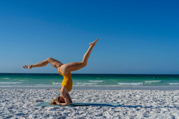 Fototapeta na wymiar A Gorgeous Blonde Fit Model Practices Yoga On A White Sand Beach In The Early Morning