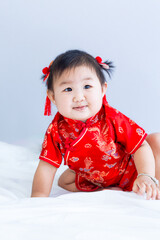 Chinese New Year concept, cute happy little girl in Chinese dress sitting in white living room. Cute Asian baby sitting in white living room, Chinese New Year concept
