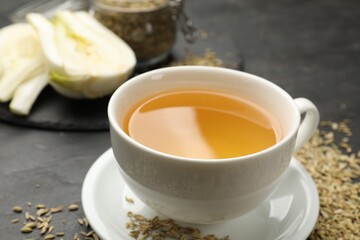 Aromatic fennel tea in cup and seeds on black table, closeup