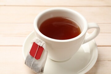 Tea bag and cup of hot beverage on light wooden table, closeup
