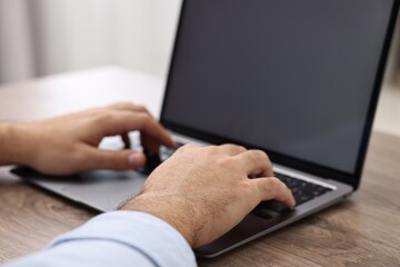 E-learning. Young man using laptop at wooden table, closeup