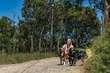 Latina woman exercising with her dogs. Woman jogging with her pets in the middle of nature. Woman walking her dogs on a sunny day. Happy dogs.