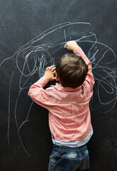Young child, scribble and art on chalkboard in classroom of preschool for education of little boy....