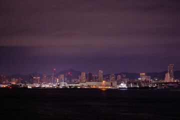 Fototapeta premium 夜の神戸の港。六甲大橋から三宮のビル街をのぞむ。背景は六甲の山並みがシルエットで浮かぶ。