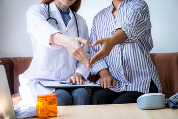 Doctor and patient woman hand do heart shape after explains the bottle of pills on the sofa at home...