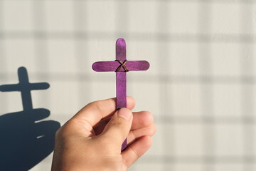 Male hand holding purple wooden cross with shadow. Christianity, faith, holy week and lent season concept.