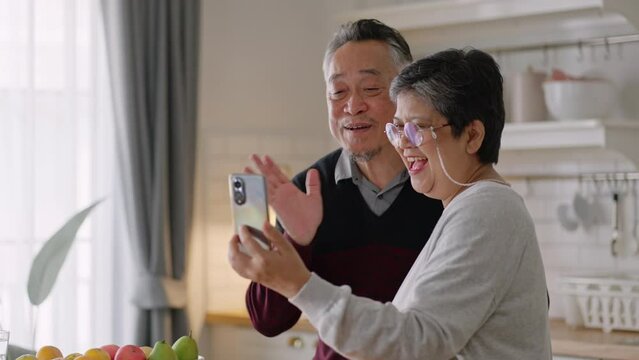 Happy asian senior elderly have fun with smartphone to talk to daughter online wave hand to webcam glad to say hello.Smiling mature male calling,app for video conversations,enjoy family retirement.