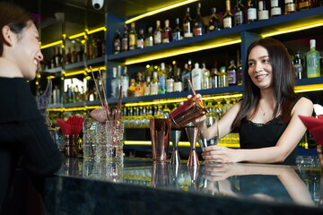 beautiful Asian woman works as a bartender standing at the counter mixing drinks and pouring beer into glasses at a party at a cocktail lounge.