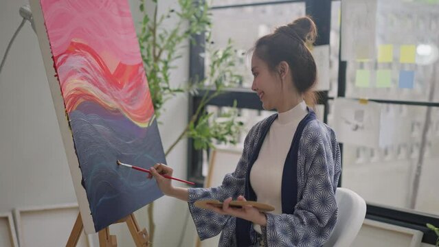 happy asian female painter using red paint on canvas,holding tube of oil paint,fine art artist drawing,asian woman painting brush on canvas.concept of enjoy leisure time with art hobby in art studio