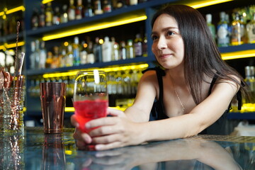 Young professional Asian bartender works behind the bar counter delivering red wine glasses to customers in a nightclub.