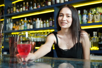Young professional Asian bartender works behind the bar counter delivering red wine glasses to customers in a nightclub.