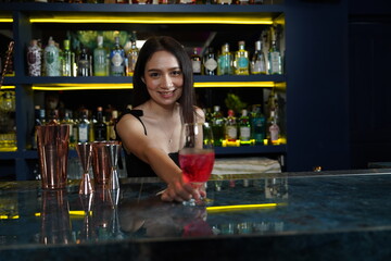 Young professional Asian bartender works behind the bar counter delivering red wine glasses to customers in a nightclub.