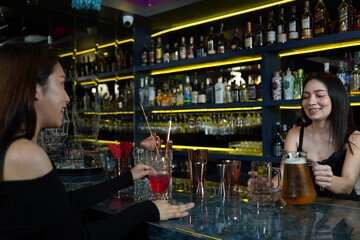 Asian woman works as a bartender, standing at the counter and pouring beer into glasses for Asian female customers to drink in the cocktail lounge.