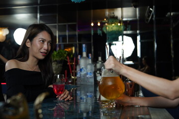 Asian woman works as a bartender, standing at the counter and pouring beer into glasses for Asian female customers to drink in the cocktail lounge.
