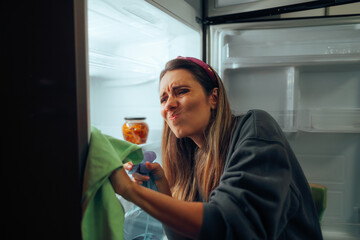 Woman Cleaning her Refrigerator Using a Special Detergent Solution. Stressed girl trying to get the...