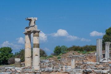 Fototapeta na wymiar Tall ancient columns stand amidst ruins under a bright clear sky