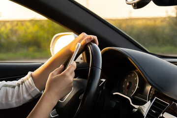 Naklejka premium Woman sending messages with smartphone while driving automobile. Female driver using mobile phone on the road during driving the car. Safety and technology concept 