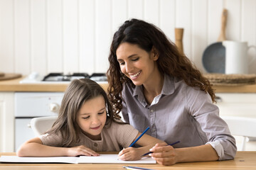 Young loving Hispanic mom spend free time with daughter sit together at table in cozy kitchen drawing in paper sketchbook with colored pencils, enjoy creative hobby, develop child on weekend at home