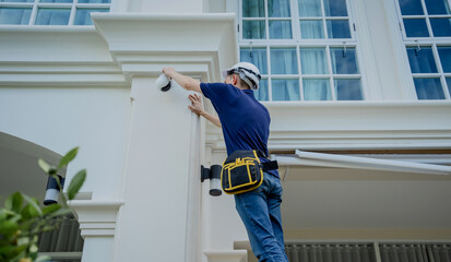 A technician installs a CCTV camera on the facade of a residential building.