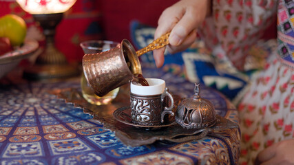 Pouring turkish coffee from cezve into cup.