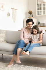 Obraz premium Preschooler girl spend time with grandmother using together modern smartphone, resting on couch enjoy new mobile application, web surfing internet, watching on-line videos, play new on-line videogame