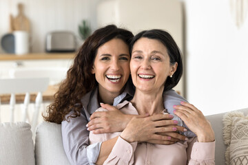 Close up portrait happy different age women hugging at home. Beautiful Hispanic female cuddling...