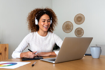 Multiracial happy female graphic designer working at home using laptop and graphic tablet.