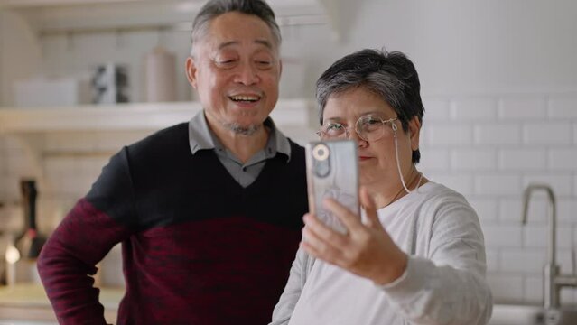 Happy asian senior elderly have fun with smartphone to talk to daughter online wave hand to webcam glad to say hello.Smiling mature male calling,app for video conversations,enjoy family retirement.