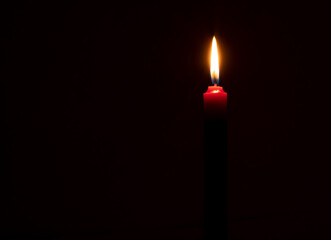 Single burning candle flame or light glowing on a small red candle on black or dark background on table in church for Christmas, funeral or memorial service with copy space