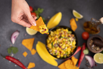 Freshly made mango salsa in a black ceramic bowl, nacho chips and ingredients
