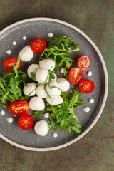 Salad with arugula, mozzarella and tomatoes in a plate on the table. Top view