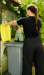 One person making a selective sorting of waste. A woman putting plastic bottles in a yellow bin for recycling.