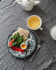 Delicious healthy brunch, breakfast - boiled egg, lightly salted salmon, arugula, chickpea crusty bread and green tea on the table, top view