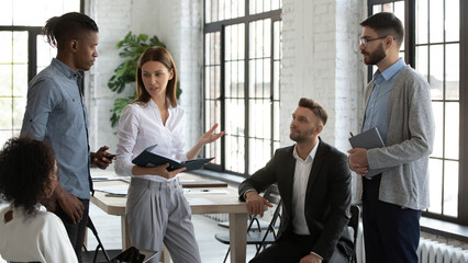Top manager talking to employees in modern loft workspace, instructing, explaining current tasks,...