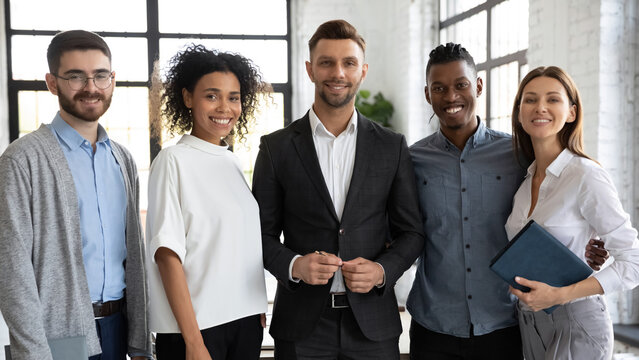 Happy colleagues at work. Aspiring young diverse coworkers smiling and looking at camera. Friendly staff members of multinational company standing close together for group photo in modern workspace
